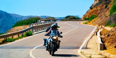 Paar auf Motorrad auf einer Küstenstrecke Sardiniens.