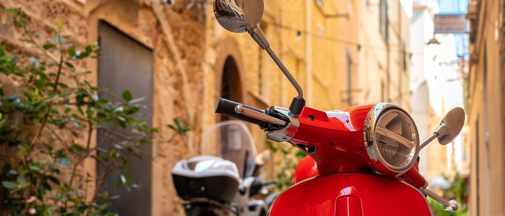 Roter Motorroller steht in einer Gasse einer italienischen Altstadt.