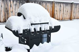 Schneebedeckter Gasgrill ohne Abdeckung im Freien.