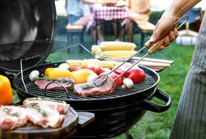 Fleisch auf einem Grill wird mit Grillzange gewendet.