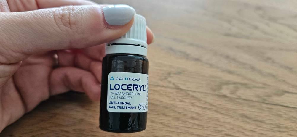 Mittel gegen Nagelpilz getestet: Eine Hand hält ein Fläschchen vor eine Holzfläche.