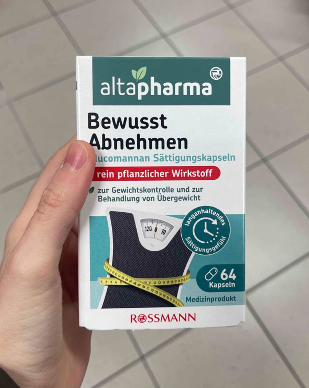 Im Test: Das Mittel zum Abnehmen in der Packung mit 64 Kapseln befindet sich in einer Hand über einem weißen Fliesenboden.