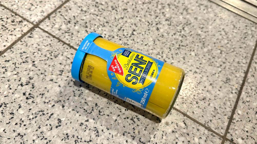 Mittelscharfer Senf im Test: Ein Glas liegt auf einem Fließenboden.