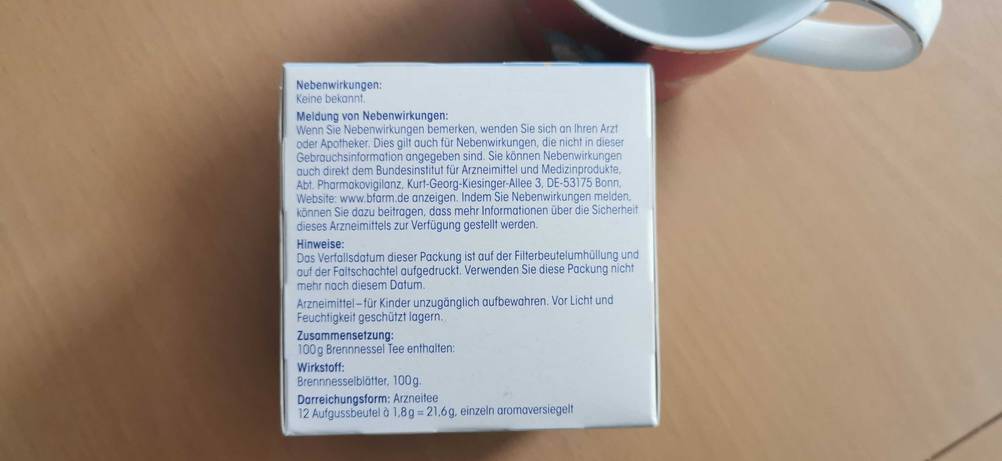 Seitenansicht einer Packung getesteten Brennnesseltees mit Informationen auf einem Holztisch.