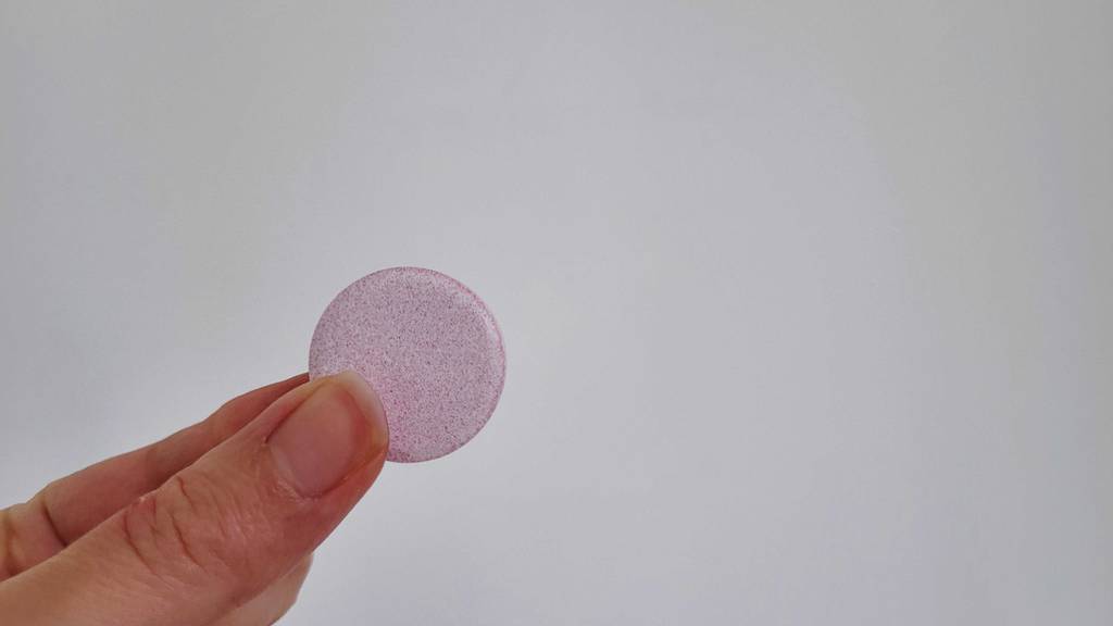 Eine Hand hält eine Brausetablette Mineralstoff zum Testen zwischen Daumen und Zeigefinger.