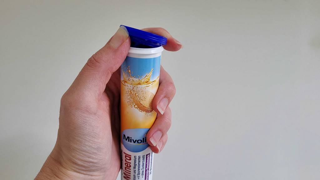 Eine Hand schnipst den Deckel einer Röhrendose mit Brausetabletten auf.