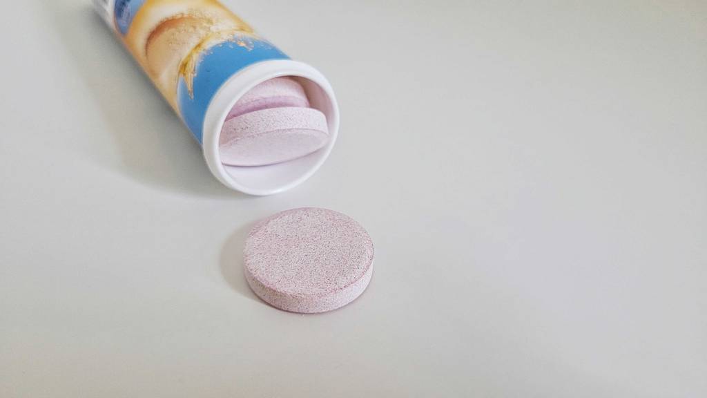 Vor einer geöffneten Röhre Brausetabletten liegt eine Tablette auf einem weißen Untergrund.