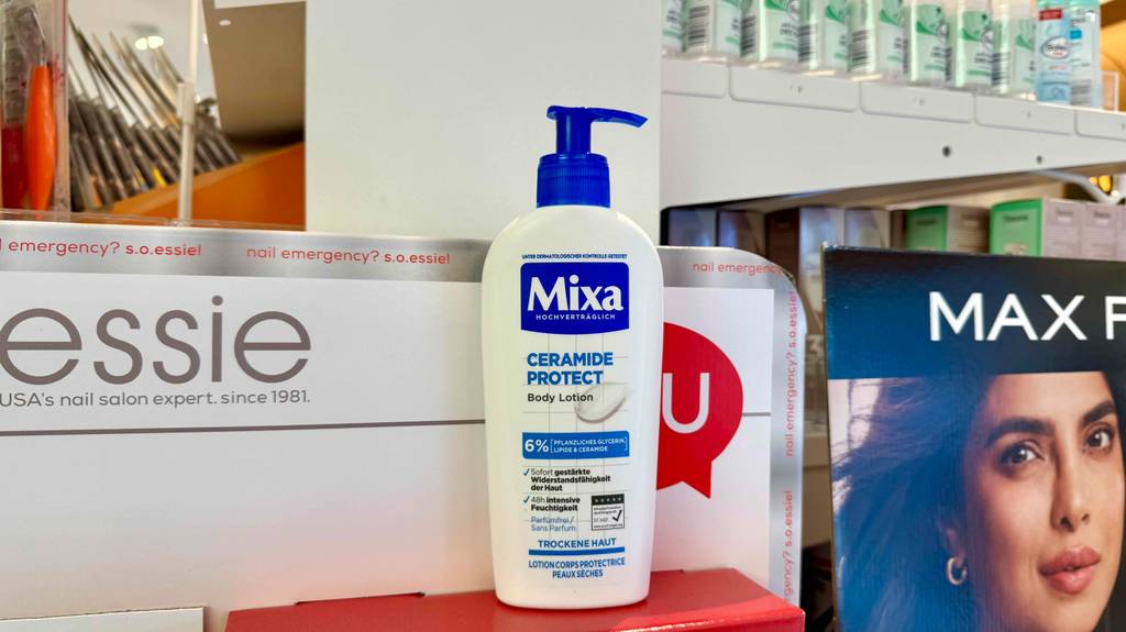 Eine Spender-Flasche mit getesteter Bodylotion für trockene Haut steht auf einem roten Karton im Drogeriemarkt.