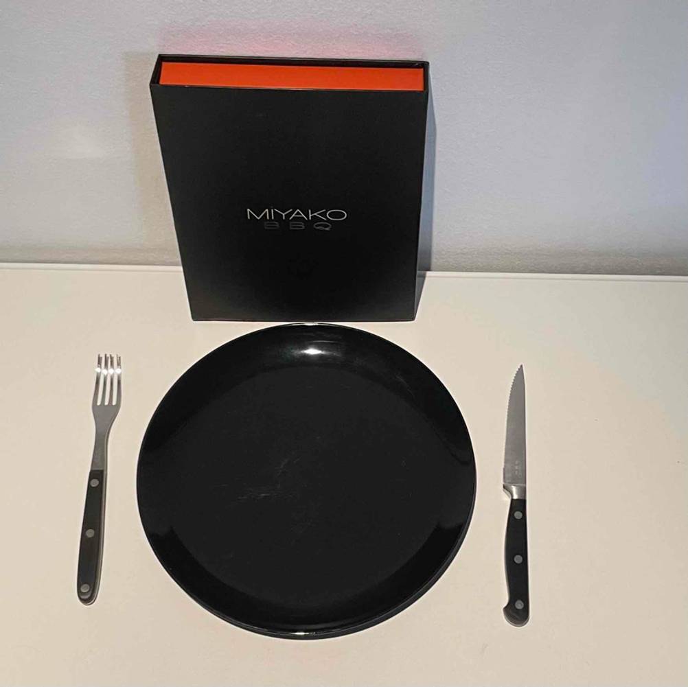 Im Test: Steakbesteck liegt links und rechts von einem schwarzen Teller, dahinter der Aufbewahrungskoffer von Miyako.