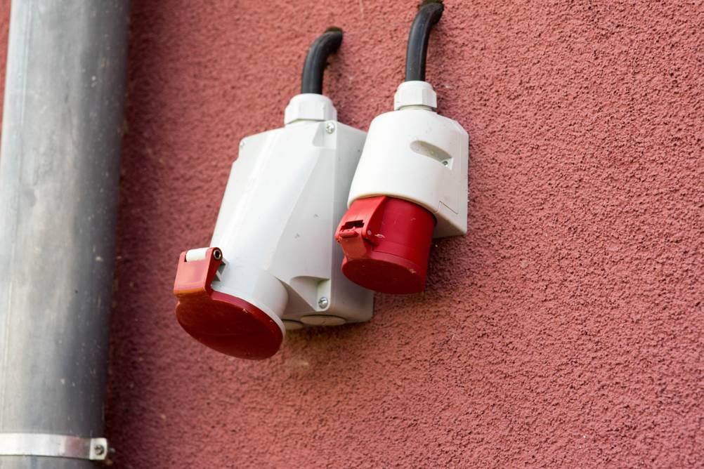 Mobile Wallbox im Test: Zwei rote Steckdosen an einer Außenwand neben einem Fallrohr.
