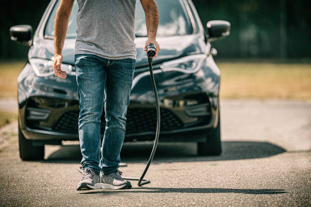 Mobile Wallbox im Test: Ein Mann geht mit einem Ladestecker in der Hand auf die Kamera zu, im Hintergrund steht ein Auto.
