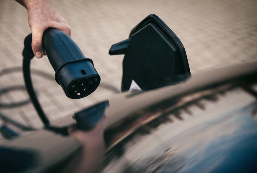 Mobile Wallbox im Test: Eine Hand hält einen Ladestecker vor die geöffnete Klappe an einem schwarzen Auto (alles nur im Anschnitt zu sehen).