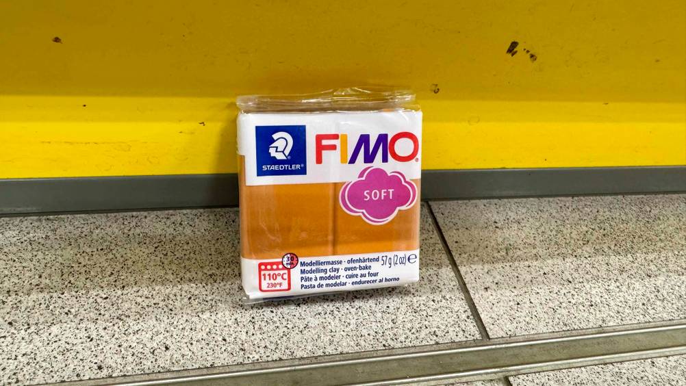 Vor einer gelben Fläche auf dem Boden steht eine Packung der getesteten Modelliermasse.