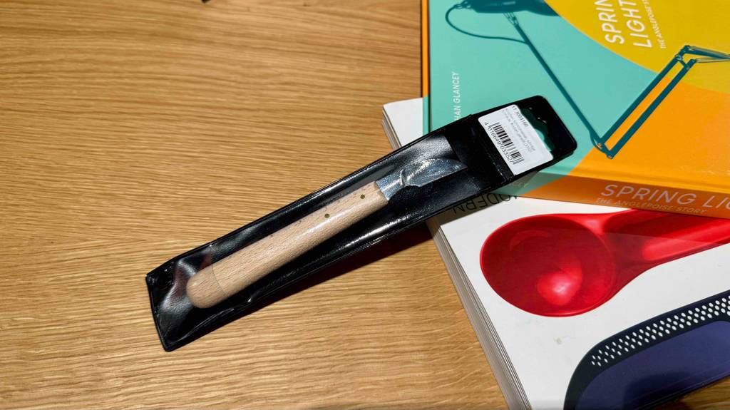 Das Schnitzmesser im Test liegt innerhalb seiner transparenten Verpackung auf zwei Büchern, die sich auf einem Holztisch befinden.