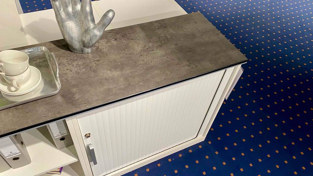 Ansicht von schräg oben auf einen weißen Jalousieschrank im Test, auf dem Dekorationsgegenstände stehen.