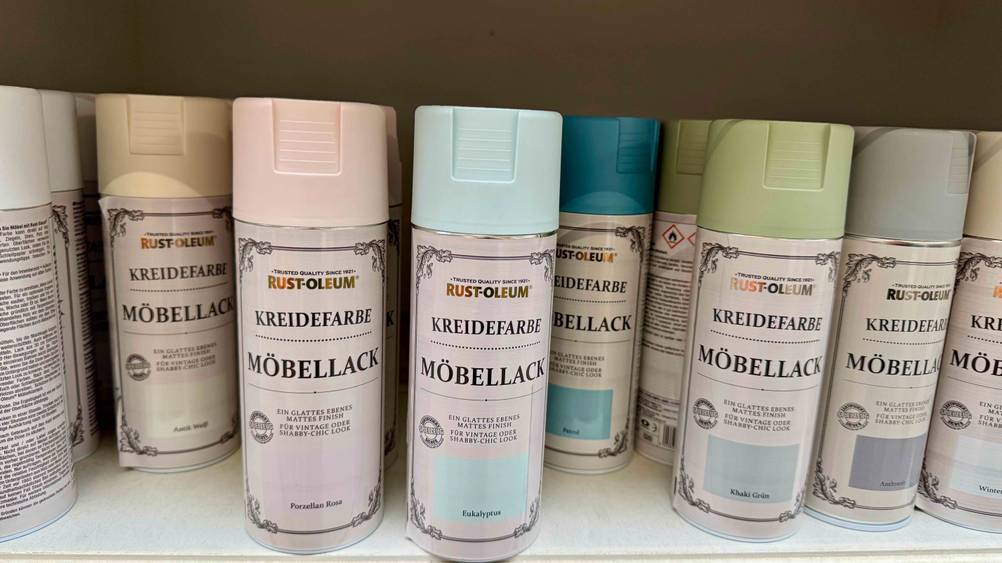 Mehrere Dosen des Möbellacks im Test in unterschiedlichen Farben in einem Verkaufsregal.