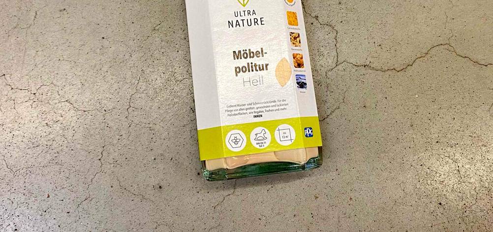 Nahaufnahme des Labels einer Flasche der getesteten Möbelpolitur von oben auf einem Betonboden liegend.
