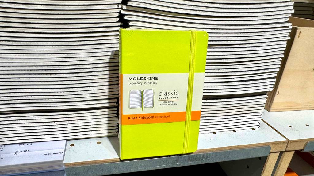 Ein gelbes Hardcover-Notizbuch steht zum testen vor mehreren gestapelten Heften.