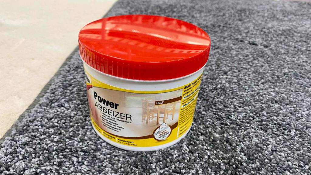 Power Abbeizer im Test: Abbeizmittel in einem weißen Tiegel mit rotem Deckel steht auf einem grau-weiß melierten Teppichboden.