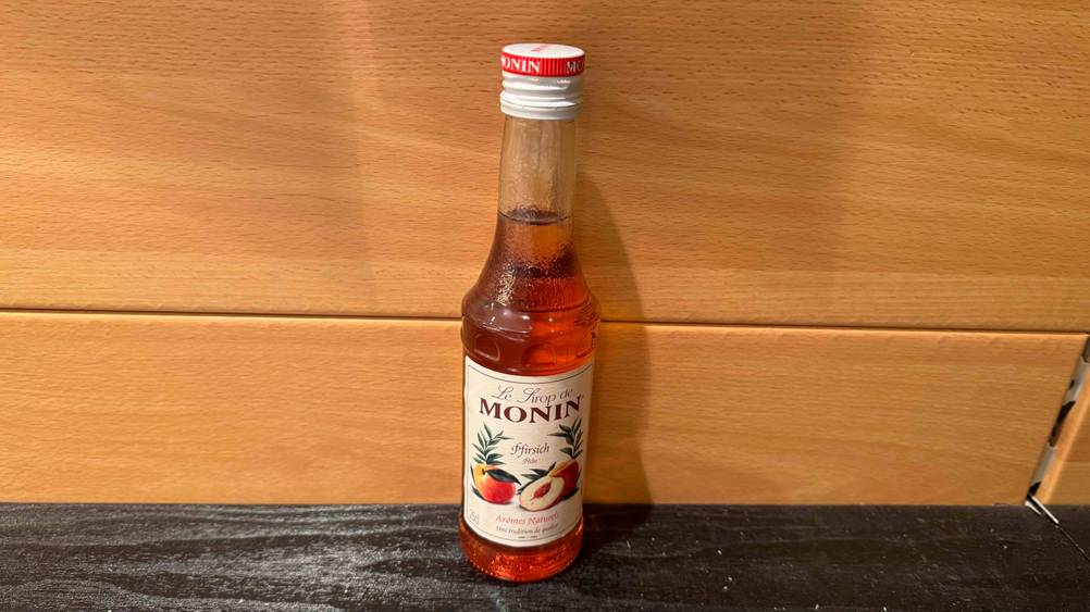 Monin-Sirup-Test: Eine Flasche von schräg oben vor einer Holzwand.