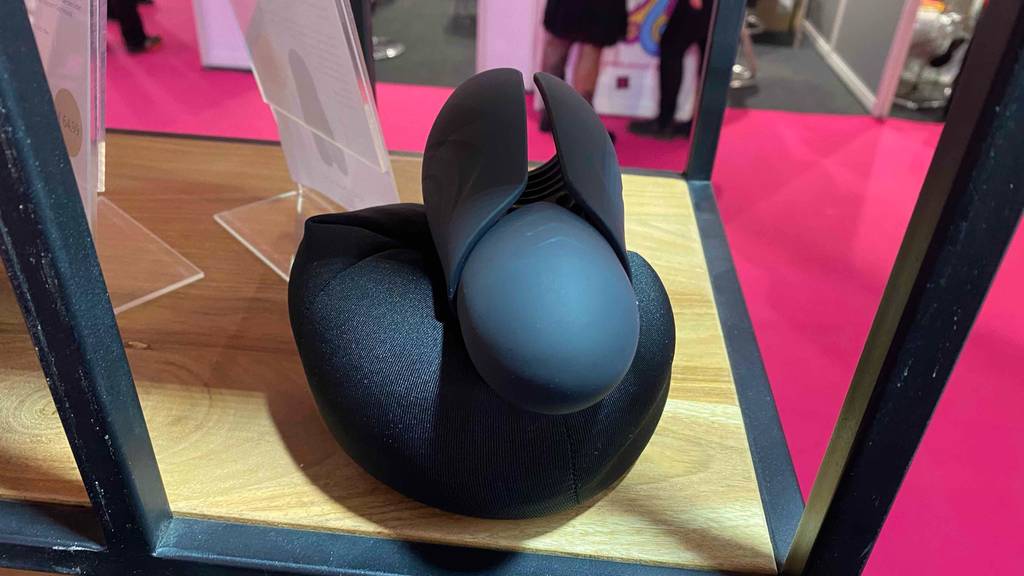 Masturbator im Test: Schwarzer Masturbator befindet sich in einem Regal aus Holz auf einem schwarzen Ausstellungskissen.