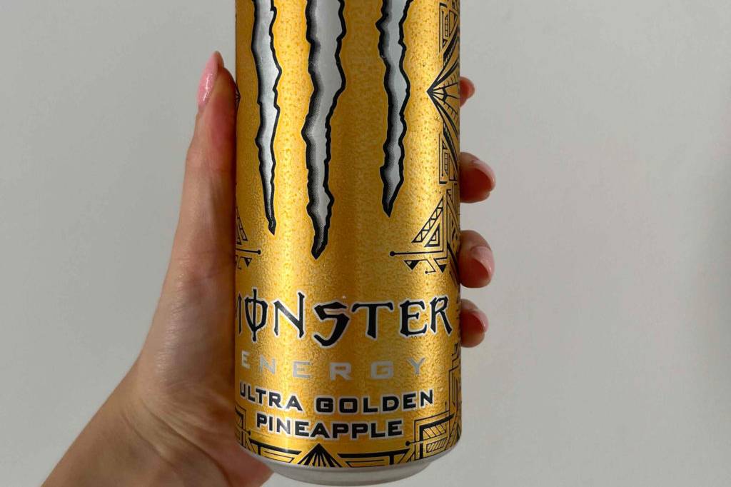 Im Test: Hand hält eine Dose Monster Energy Drink vor einer weißen Wand.