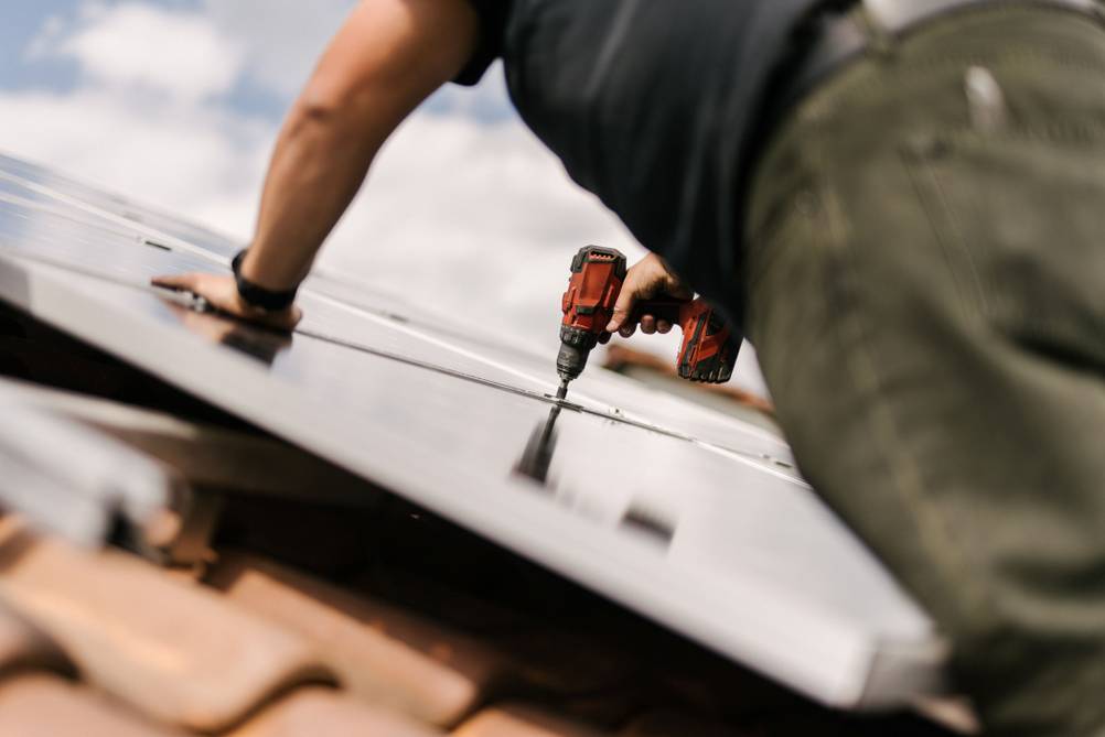 Ein Handwerker montiert eine PV-Anlage auf dem Dach eines Hauses.