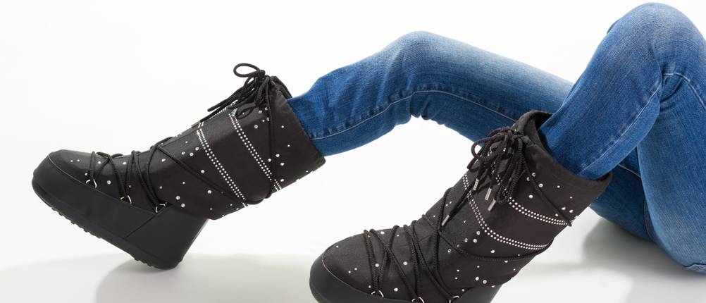 Moon Boots im Test: Frau liegt mit schwarzen Moon Boots und blauer Jeans auf dem Boden.