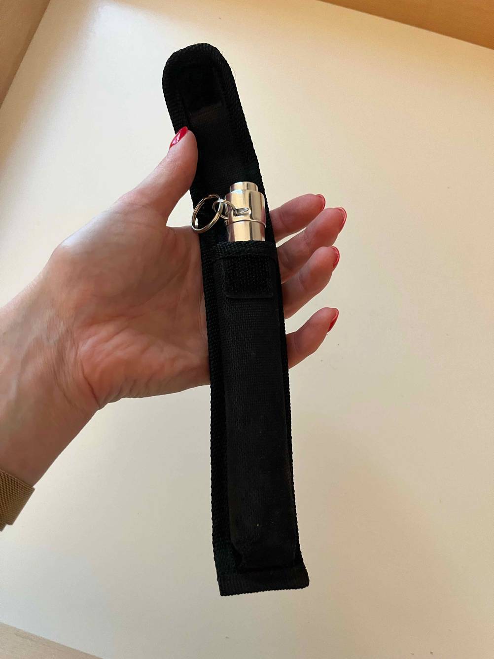 Hand hält einen schwarzen Verpackungsbeutel, aus der eine getestete Mini-Taschenlampe herausragt.