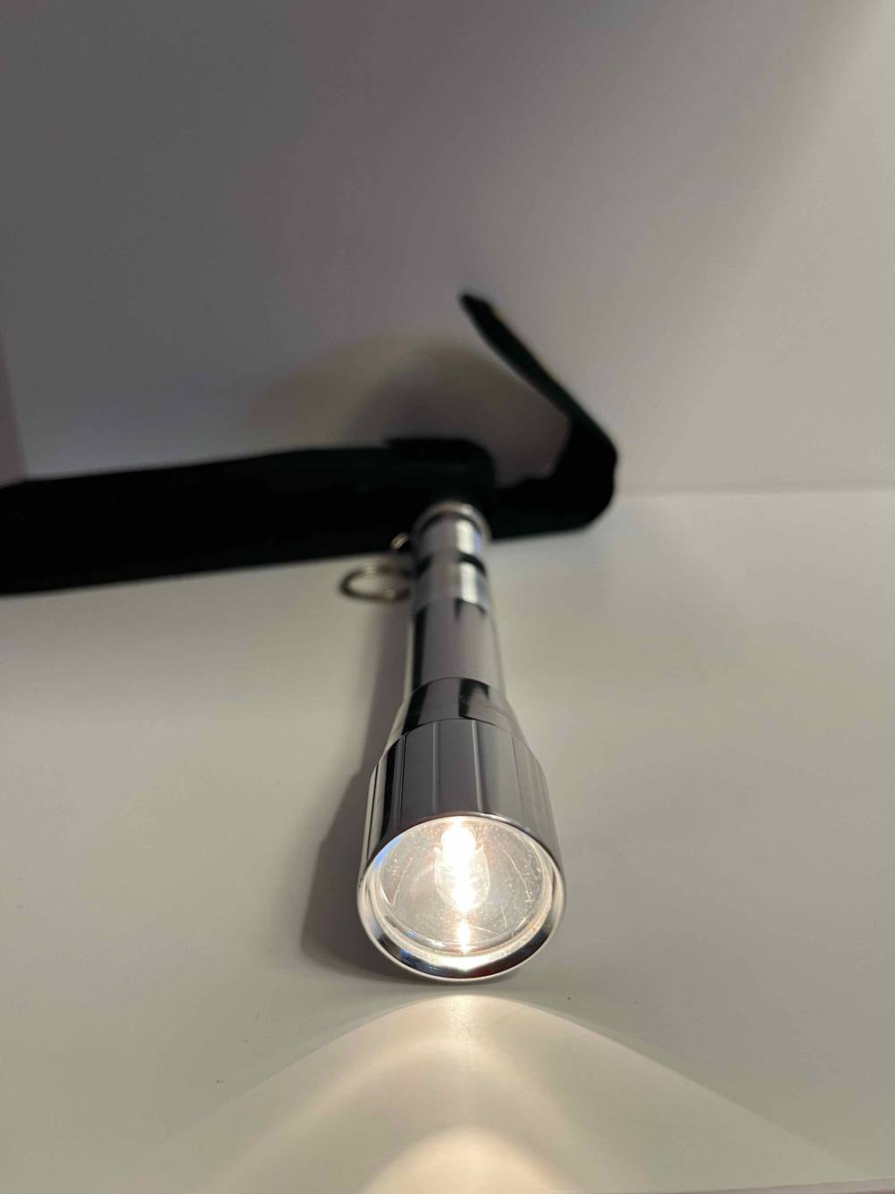 Getestete leuchtende Mini-Taschenlampe liegt vor Verpackungstasche in weißem Regal.