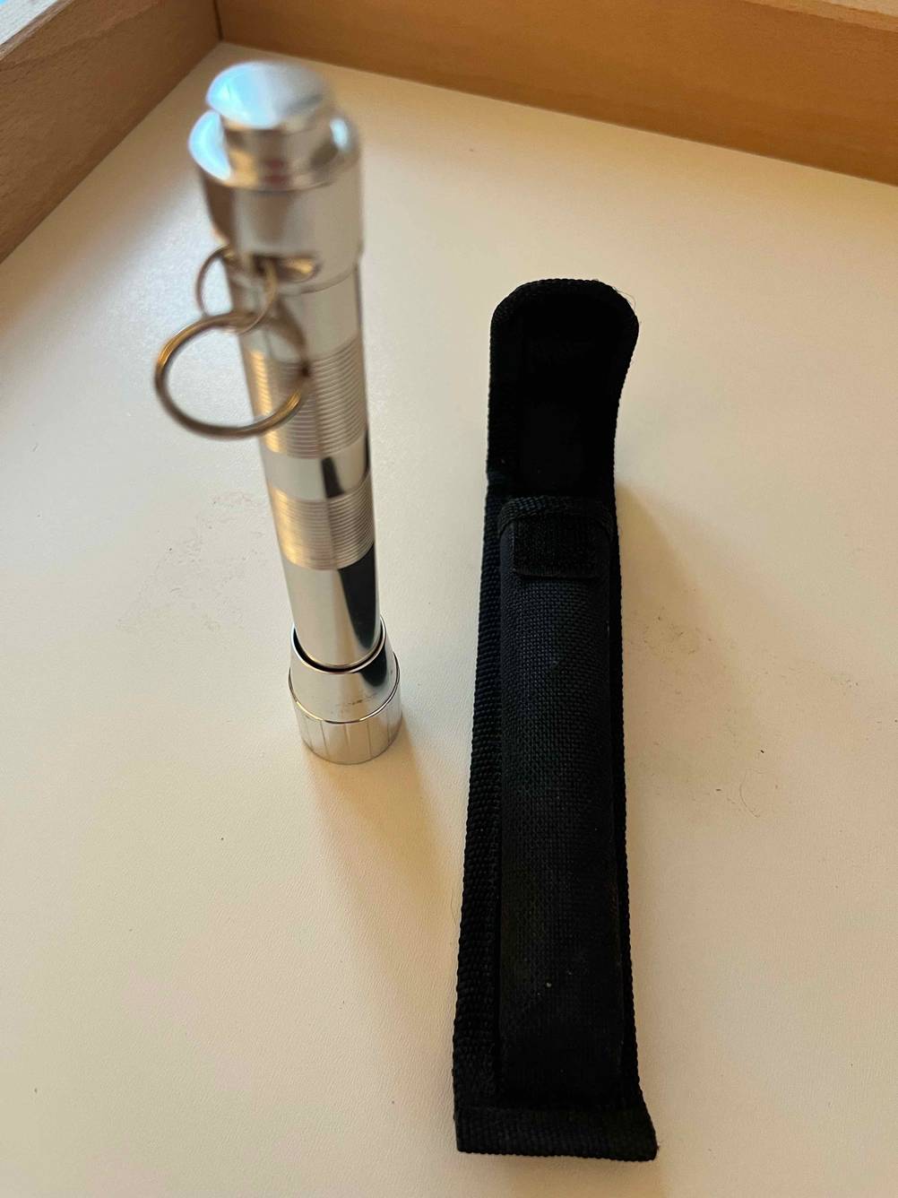 Getestete Mini-Taschenlampe steht neben schwarzem Verpackungsbeutel auf weißer Fläche.