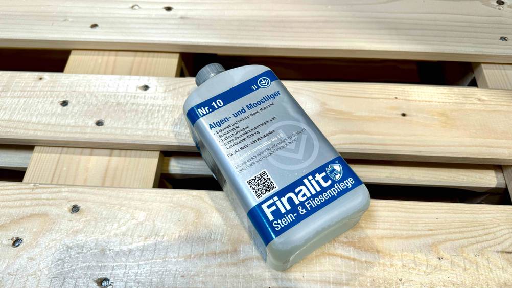 Eine Flasche des getesteten Moosentferners liegt auf einer Palette.