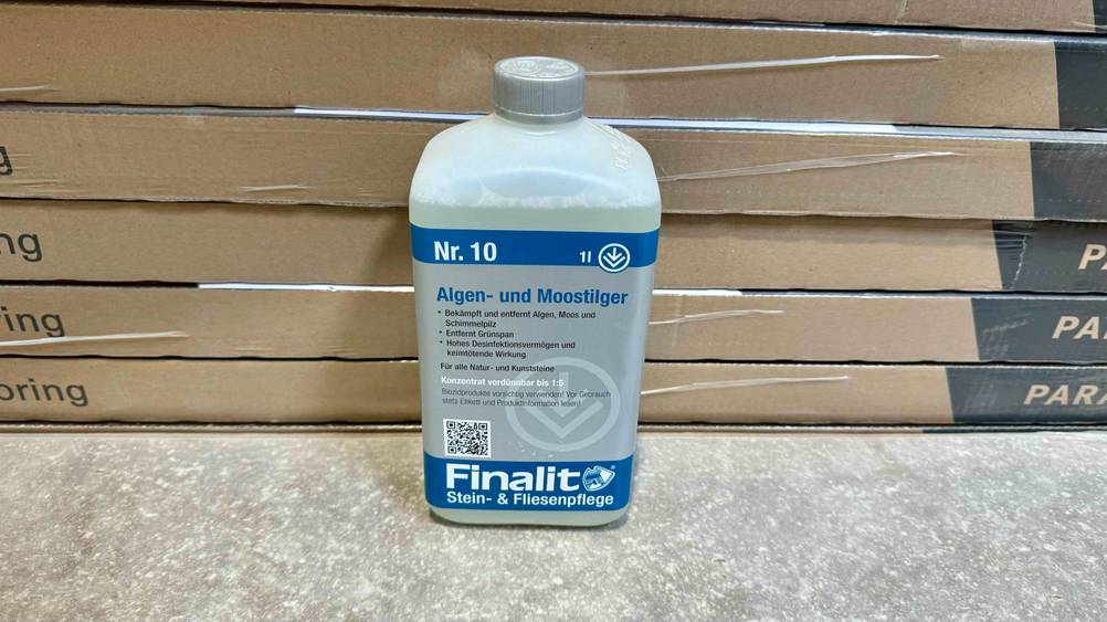 Moosentferner getestet: Eine Flasche vor mehreren Kartonagen auf einem Betonboden.