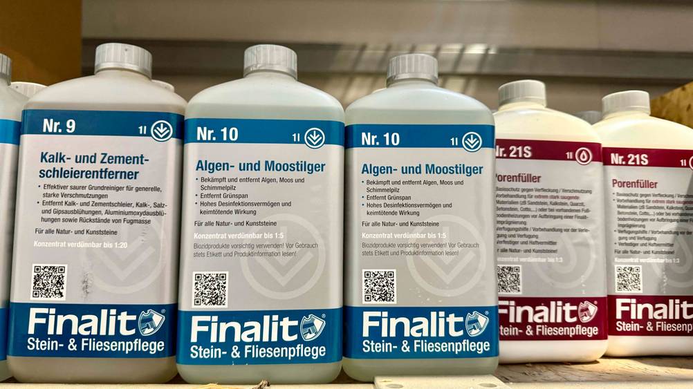 Mehrere Flaschen des Moosentferners im Test neben anderen Produkten im Regal.