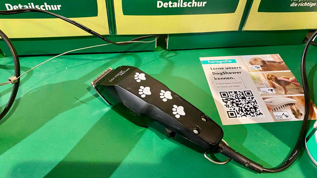 Profi-Hundeschermaschine im Test: Ein Gerät mit Pfotendesign liegt auf einer grünen Fläche neben dem Infoflyer.