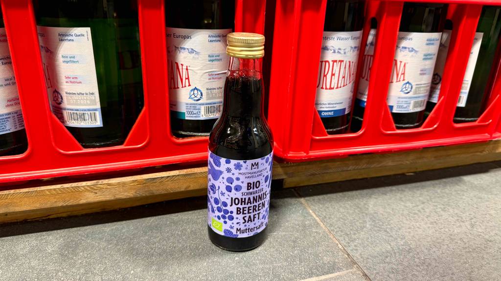 Getesteter Johannisbeersaft in der Flasche steht vor roten Wasserkästen im Geschäft.
