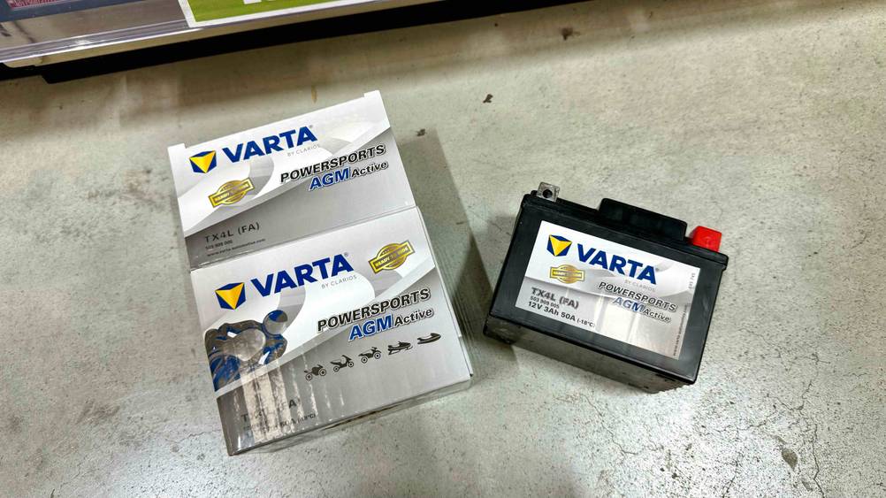 Neben der Originalverpackung liegt die getestete Motorrad-Batterie auf einem Betonboden.