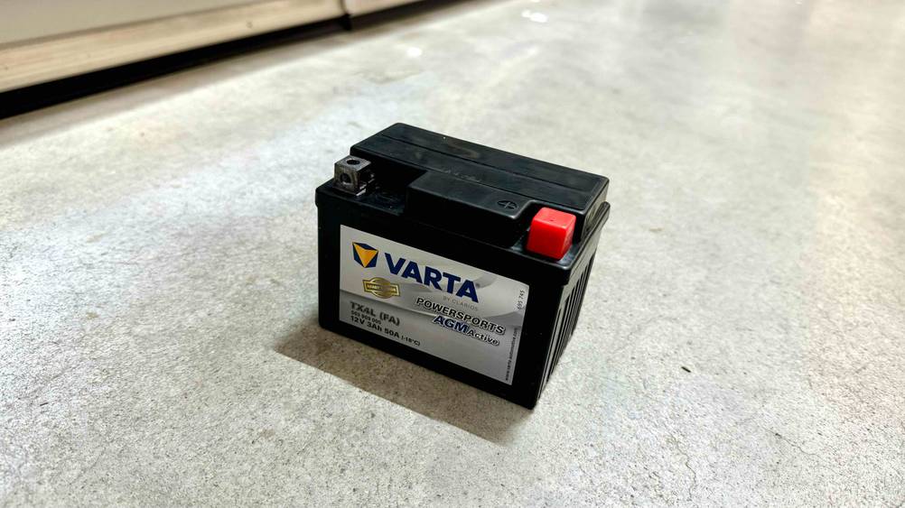 Eine Motorrad-Batterie im Test von schräg oben auf einem Betonboden.