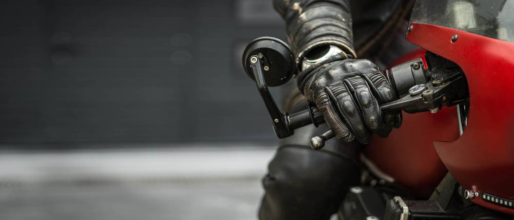 Behandschuhte Hand auf dem Lenker eines Motorrads.