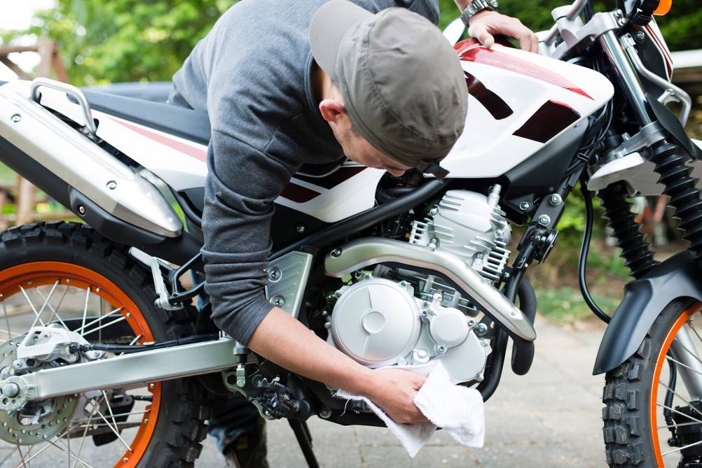 Ein Mann ist über sein Motorrad gebeugt. Er reinigt mit einem Tuch Teile des Motorrads.