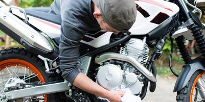 Ein Mann ist über sein Motorrad gebeugt. Er reinigt mit einem Tuch Teile des Motorrads.