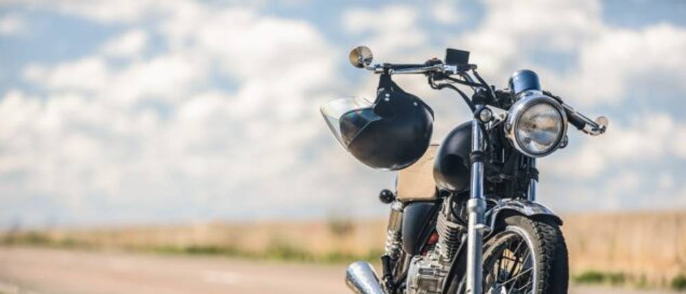 Motorrad parkt auf einer Straße und ein Helm hängt am Lenker.