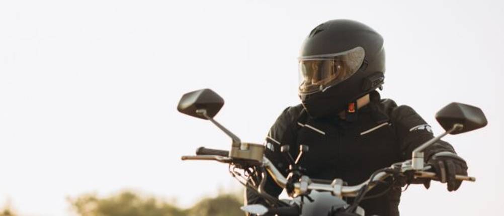 Mann mit Motorradhelm sitzt auf einem Motorrad und sieht zur Seite.