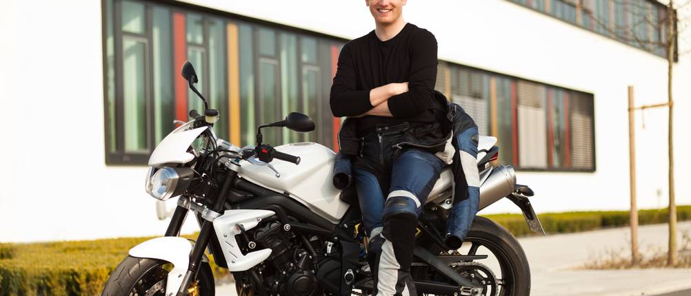 Ein junger Mann steht in Schutzkleidung vor seinem Motorrad.