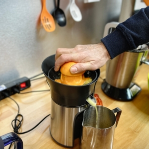 Eine Hand drückt eine halbe Orange auf den Presskegel der Moulinex PC603D10. Der frische Saft läuft in ein Edelstahlgefäß.