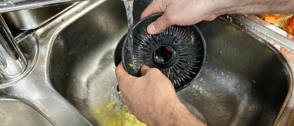 Ein Sieb-Einsatz der Moulinex PC603D10 wird unter fließendem Wasser in der Spüle gereinigt. Reste von Fruchtfleisch sind noch sichtbar.