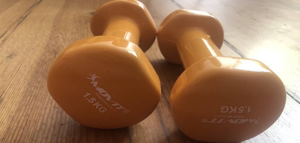 zwei gelbe 1,5 kg Hanteln liegen auf einem Holzboden