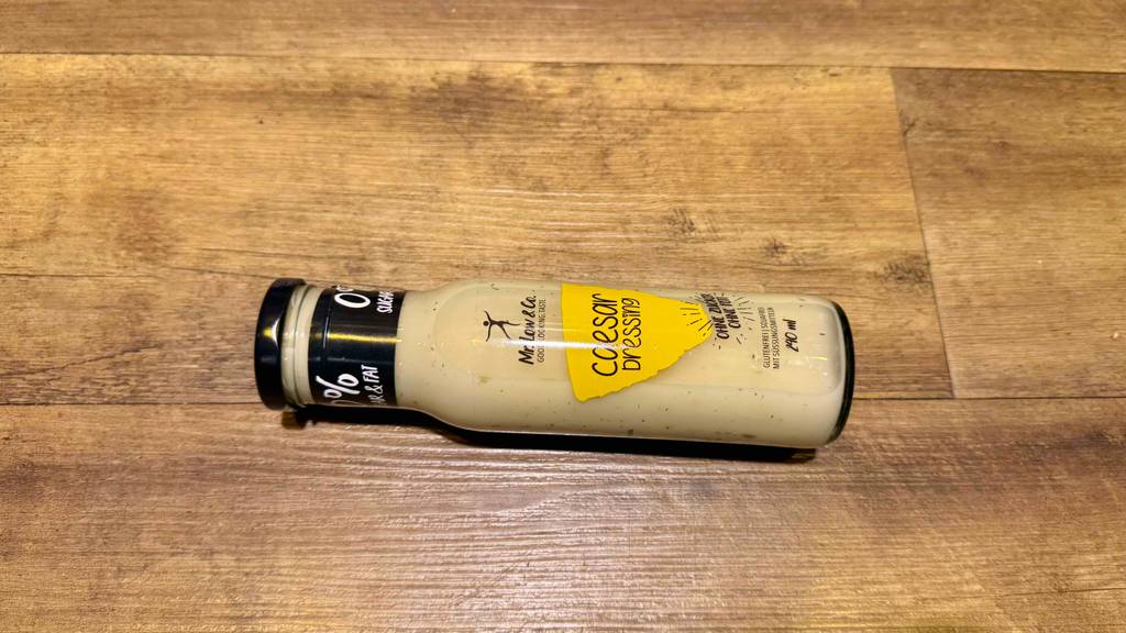 Im Test: Caesar-Dressing in der 240-ml-Flasche liegt auf einer Holzoberfläche.