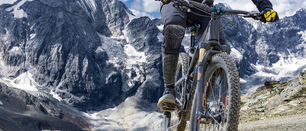 MTB-Fully Test: Ein Mann in Schutzbekleidung fährt auf einem MTB Fully, im Hintergrund zu sehen ist eine Bergkulisse.