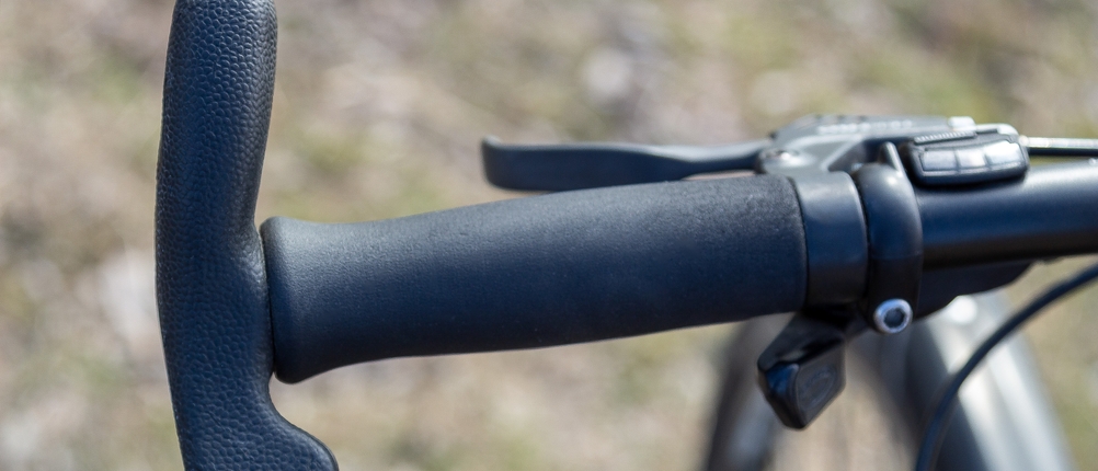 Ein Fahrradlenker mit ergonomischen Bar Ends, die eine zusätzliche Handposition ermöglichen. Der Hintergrund zeigt einen leicht unscharfen Naturpfad.